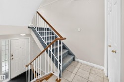 Foyer featuring a white paneled entry door with sidelight, tile flooring, and carpeted stairs with white balusters and wood handrails - 