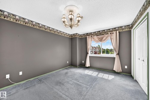 Spacious room featuring a central chandelier with decorative ceiling medallion, neutral gray walls, and light blue carpeting - 51 9630 176 Street, Edmonton, AB 