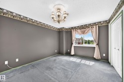 Spacious room featuring a central chandelier with decorative ceiling medallion, neutral gray walls, and light blue carpeting - 