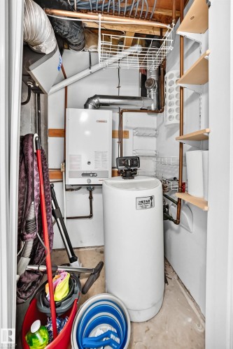 Utility closet featuring a wall-mounted tankless water heater, water softener system, copper piping, and open shelving - 51 9630 176 Street, Edmonton, AB 