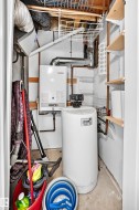 Utility closet featuring a wall-mounted tankless water heater, water softener system, copper piping, and open shelving - 