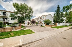 Entryway featuring a stone-clad monument sign, wrought iron accents, and mature landscaping - 
