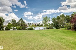 Expansive green lawn with mature trees and a tranquil body of water in the background - 