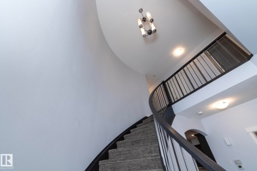 Curved staircase with carpeted treads and dark wood-finish handrail, featuring black metal balusters - 2016 Redtail Common, Edmonton, AB 