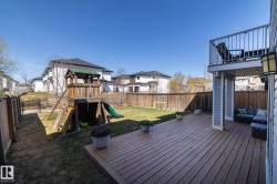 Spacious rear yard featuring a wood deck, upper-level balcony with metal railing, and a fenced perimeter - 