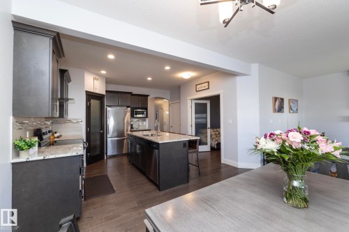 Open-concept kitchen featuring dark wood-finish cabinetry, stainless steel appliances, a center island with a sink, and light-toned countertops - 2016 Redtail Common, Edmonton, AB 