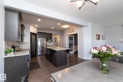 Open-concept kitchen featuring dark wood-finish cabinetry, stainless steel appliances, a center island with a sink, and light-toned countertops - 