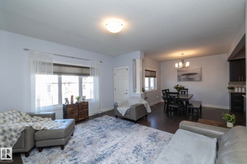 Open-concept living space featuring dark wood-finish flooring, recessed lighting, and a dining area with a four-light chandelier - 2016 Redtail Common, Edmonton, AB 