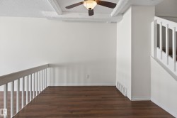 Open loft area featuring wood-finish flooring, a white spindle railing, and a ceiling fan with light - 