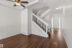 Open-concept interior featuring wood-finish flooring throughout, a multi-level staircase with white balusters, and a contemporary ceiling fan with integrated lighting - 