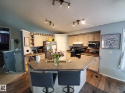 Open-concept kitchen featuring an eat-at island, ample cabinetry, and wood-finish flooring - 
