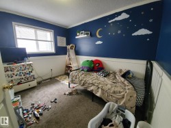 Bedroom featuring a large window with white blinds, dark blue painted walls with a decorative celestial mural, and white wainscoting - 