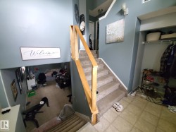 Carpeted staircase with natural wood railing, leading to a lower level with carpeted flooring - 
