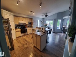 Open-concept kitchen featuring light wood-finish cabinetry, stainless steel appliances, a kitchen island with seating, and wood-finish flooring - 