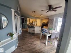 Open-concept living space featuring wood-finish flooring, a kitchen island with seating, a dining area, and a ceiling fan - 