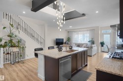 Open-concept living space featuring wood-finish flooring throughout, a modern island kitchen with an undermount double sink, stainless steel appliances, and granite countertops - 