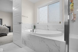 Contemporary bathroom featuring a built-in oval soaking tub with deck-mounted fixtures, white marble-look tile surround, and a frosted window - 