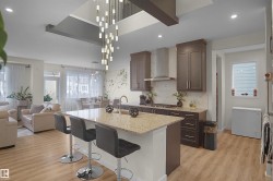 Open-concept kitchen featuring an oversized island with a granite countertop, stainless steel appliances, dark wood cabinetry, and a full-height backsplash - 