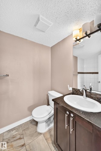 Bathroom featuring a dark wood-finish vanity with a white oval sink, dark countertop, and a contemporary two-light fixture - 308 18126 77 Street, Edmonton, AB 