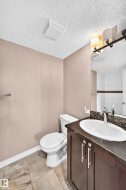 Bathroom featuring a dark wood-finish vanity with a white oval sink, dark countertop, and a contemporary two-light fixture - 