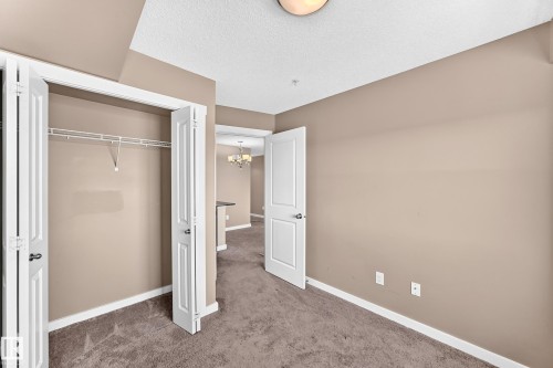 Carpeted room featuring a double bi-fold closet with shelving, neutral wall paint, white trim, and a semi-flush ceiling light - 308 18126 77 Street, Edmonton, AB 
