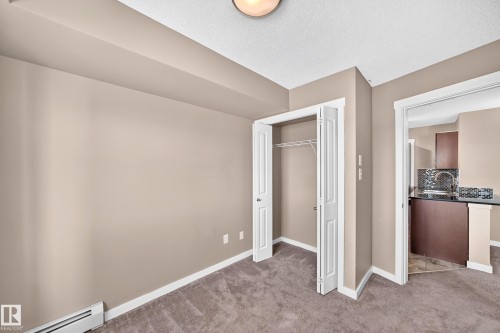 Carpeted room with neutral-toned walls, featuring a bi-fold door closet with wire shelving - 308 18126 77 Street, Edmonton, AB 