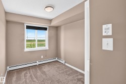 Carpeted room featuring a white-framed window with a black roller blind, baseboard heating, a ceiling-mounted light fixture, and neutral wall paint - 