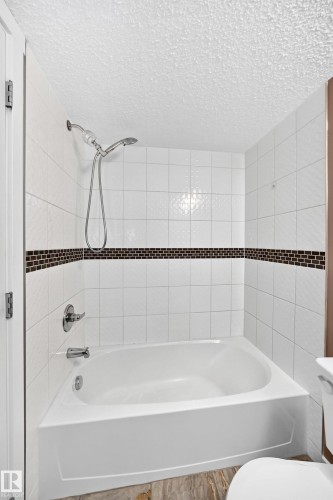White tiled bathtub and shower combination featuring chrome fixtures and a decorative mosaic accent tile band - 308 18126 77 Street, Edmonton, AB 
