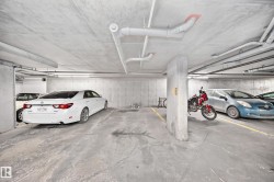 Concrete parking garage with exposed ceiling pipes, fluorescent strip lighting, and painted yellow parking lines - 