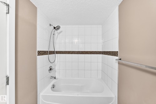 Bathtub and shower combination featuring white subway tile, a decorative mosaic tile accent band, and chrome fixtures - 308 18126 77 Street, Edmonton, AB 