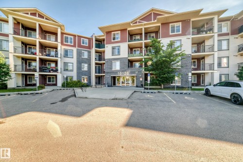 Multi-story residential building featuring a stone and siding exterior, multiple private balconies with black railings, and a prominent main entrance - 308 18126 77 Street, Edmonton, AB 