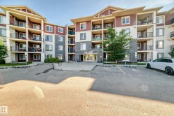 Multi-story residential building featuring a stone and siding exterior, multiple private balconies with black railings, and a prominent main entrance - 