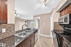 Kitchen featuring dark wood cabinetry, a dual-basin stainless steel sink, black countertops, and a mosaic tile backsplash - 