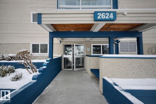 Building entrance featuring a covered walkway, glass doors, and a blue accent trim - 107, 2624 Millwoods Road East Nw, Edmonton, AB - Outdoor With Exterior