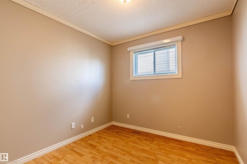 Bedroom featuring light beige walls, wood-finish flooring, white baseboards, and crown molding - 3 Glenforest Crescent, Stony Plain, AB 