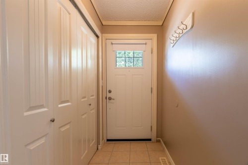 Entryway featuring a paneled door with decorative glass, beige floor tiles, and bi-fold closet doors - 3 Glenforest Crescent, Stony Plain, AB 