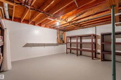 Basement storage space featuring exposed wood joists, painted concrete floor, built-in shelving units, and a visible electrical panel - 
