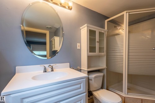 Bathroom featuring a glass-enclosed shower, white vanity with integrated sink, oval wall mirror, chrome fixtures, and an over-toilet storage cabinet - 3 Glenforest Crescent, Stony Plain, AB 