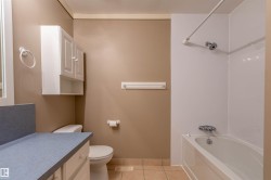 Bathroom featuring a white bathtub with an integrated shower, a toilet, and a vanity with a laminate countertop - 