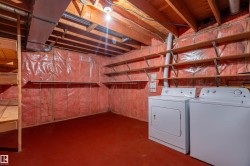 Basement utility space featuring a washer and dryer, red flooring, exposed wood ceiling joists, and extensive wall shelving - 