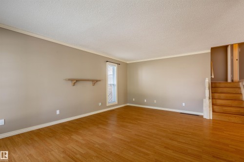 Spacious room featuring wood-finish flooring, neutral-toned walls, and white crown molding - 3 Glenforest Crescent, Stony Plain, AB 