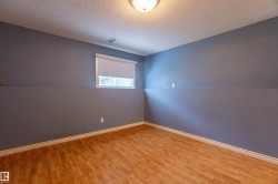 Room featuring wood-finish flooring, light blue and gray painted walls, a window with a roller blind, white baseboards, and a flush-mount ceiling light fixture - 