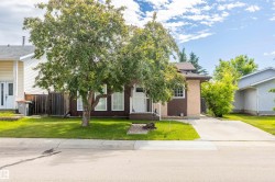 Split-level residence featuring a brown and stucco exterior, white window trim, and a concrete driveway - 