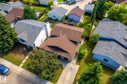 Brown shingle roofing with a prominent chimney, concrete driveway, and a front yard with mature trees - 