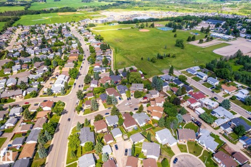 Aerial perspective of a residential community with single-family homes, surrounding green spaces, and a recreational field with sports courts - 3 Glenforest Crescent, Stony Plain, AB 