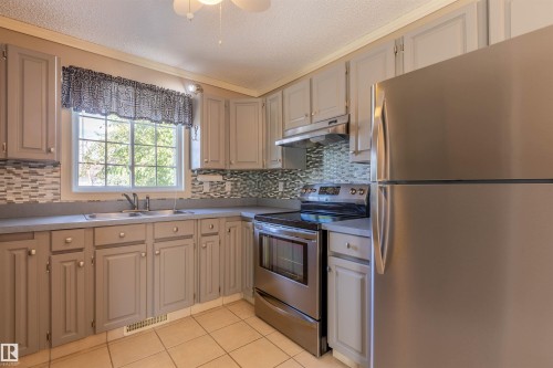 Kitchen featuring light gray cabinetry, stainless steel appliances, mosaic tile backsplash, and light-toned tile flooring - 3 Glenforest Crescent, Stony Plain, AB 