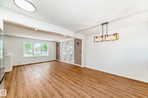Spacious interior featuring wood-finish flooring, a decorative accent wall with marble-style panels, and a modern chandelier - 4842 116Ave, Edmonton, AB - Indoor Photo Showing Other Room