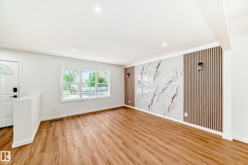 Spacious interior featuring wood-finish flooring, a wall accent with marble-effect panels and vertical slat detailing, and recessed lighting - 4842 116Ave, Edmonton, AB - Indoor Photo Showing Other Room