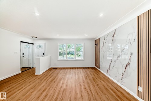 Spacious room featuring wood-finish flooring, a decorative accent wall with a marble-effect panel, and a slat wood panel accent - 4842 116Ave, Edmonton, AB - Indoor Photo Showing Other Room