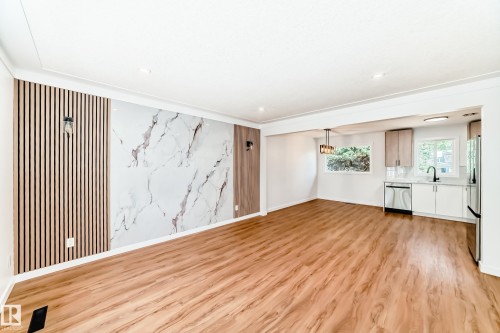 Open-concept living area featuring wood-finish flooring, a decorative wall panel with vertical wood slats and a marble-patterned inlay, and recessed lighting - 4842 116Ave, Edmonton, AB - Indoor